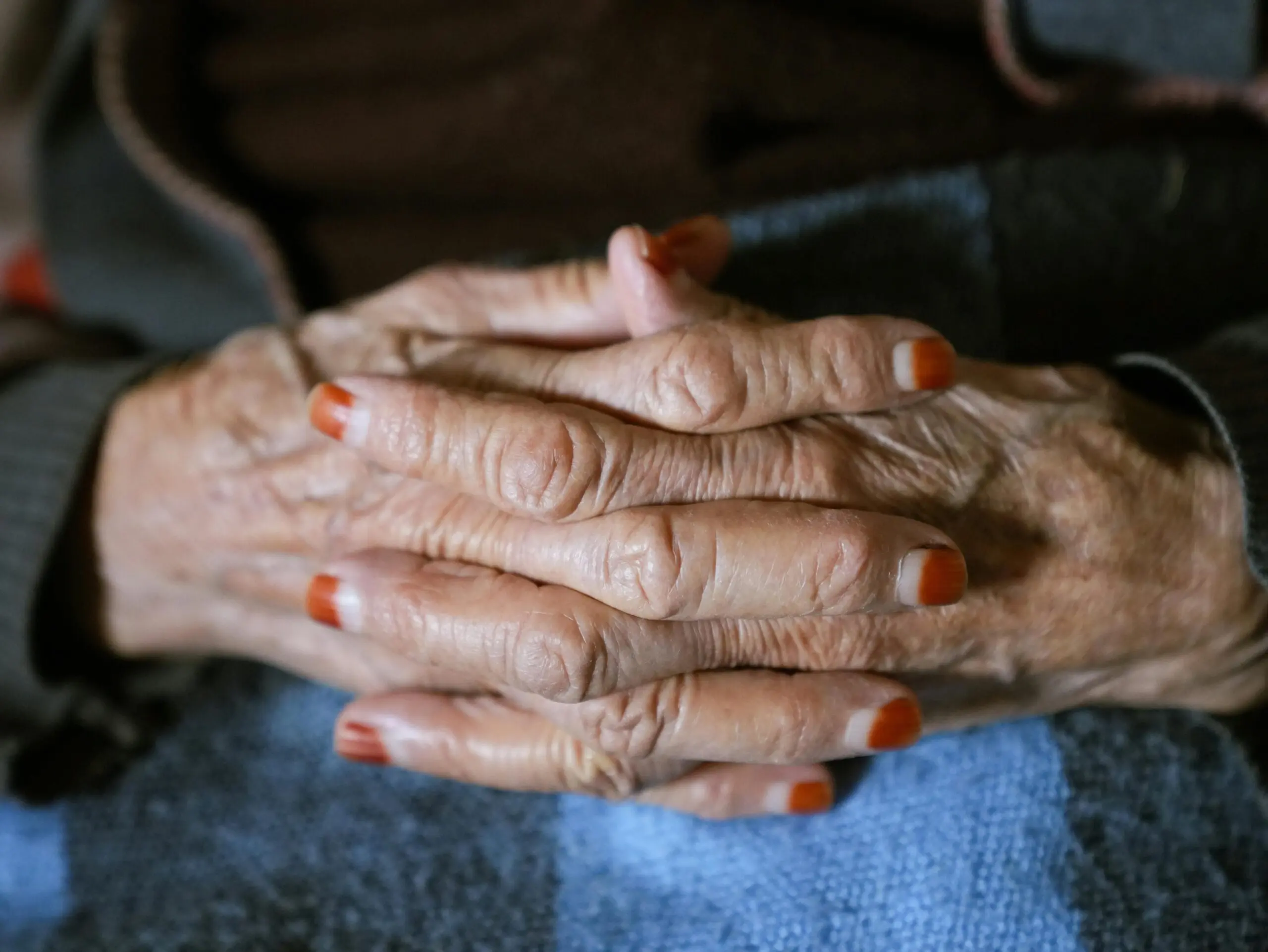 Detailed view of senior adult hands with painted nails crossed gently, conveying warmth and wisdom.