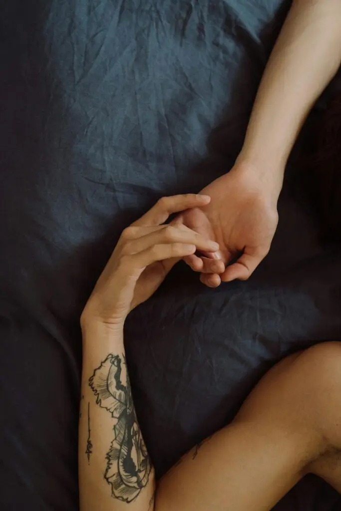 A tattooed arm holding hands in an intimate setting, symbolizing love and tenderness.