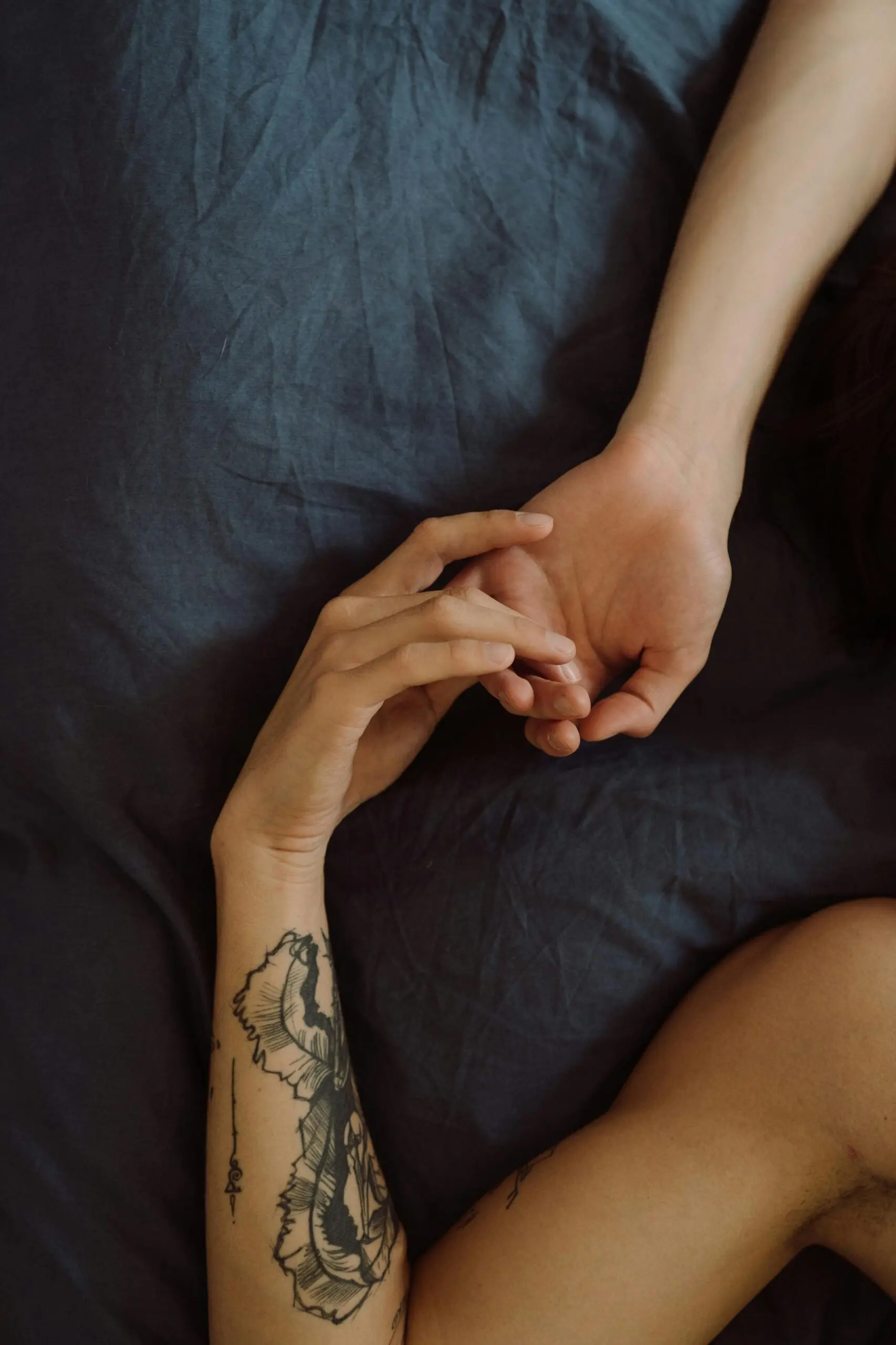 A tattooed arm holding hands in an intimate setting, symbolizing love and tenderness.