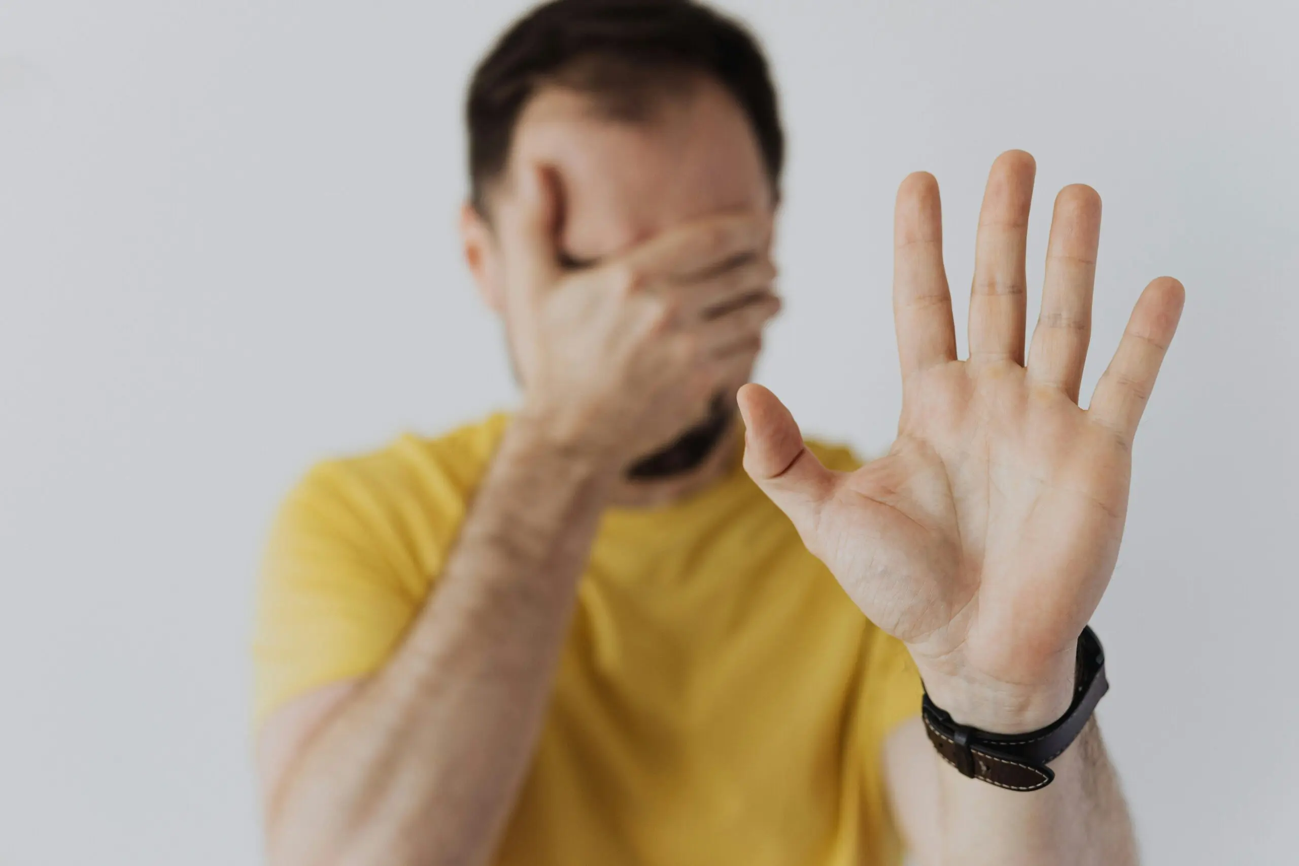 Close-up of a man covering his face and showing a stop gesture with his hand.