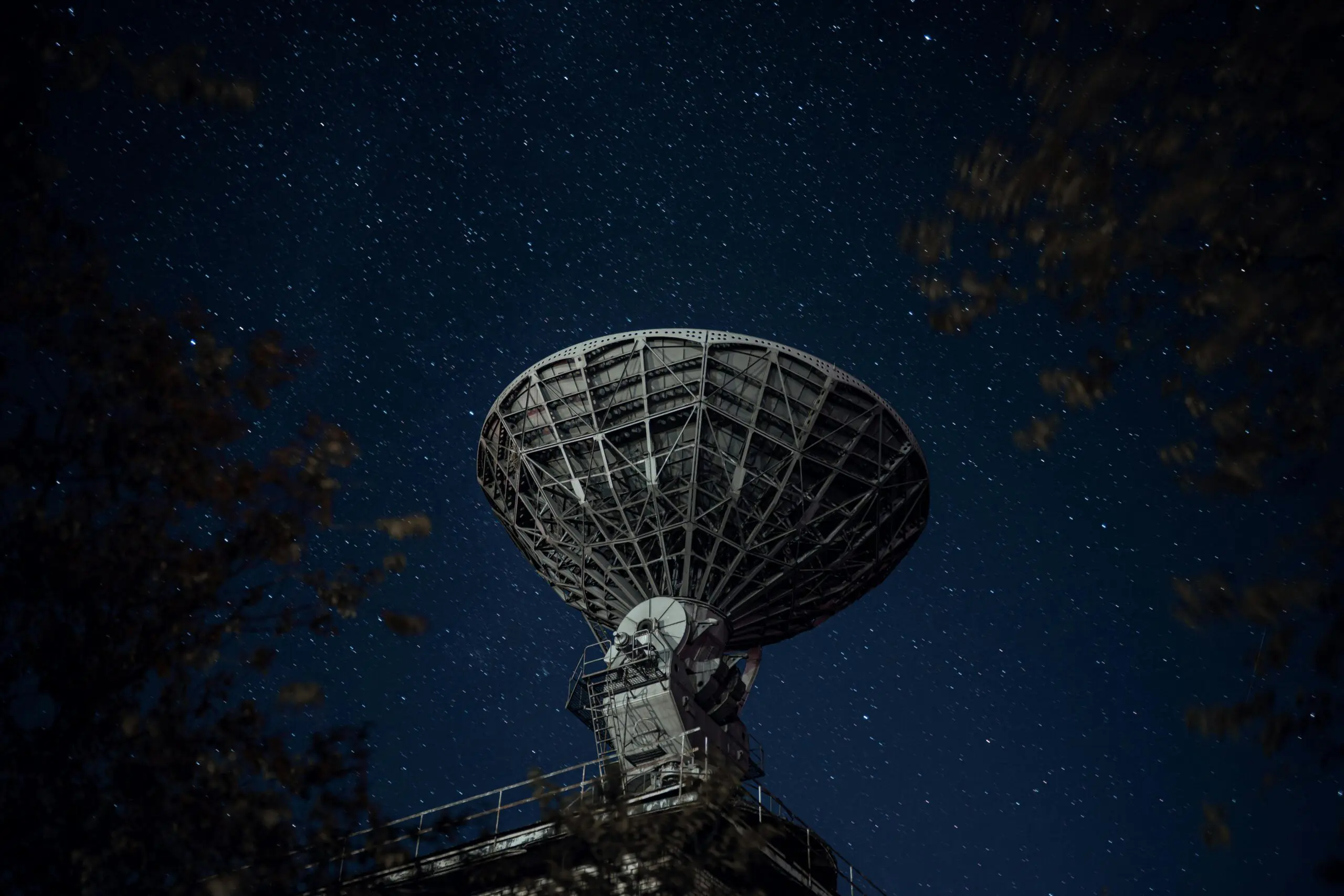 A large radio telescope beneath a starry night sky capturing celestial signals.