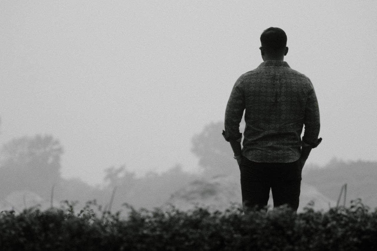 A lone man stands in a foggy landscape, evoking solitude and contemplation.